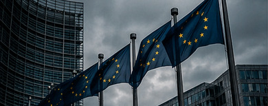 European Union flags flying outside glass institutional buildings under a dark sky.